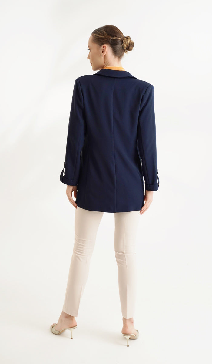 back view of woman wearing a navy blue blazer with cream pants.