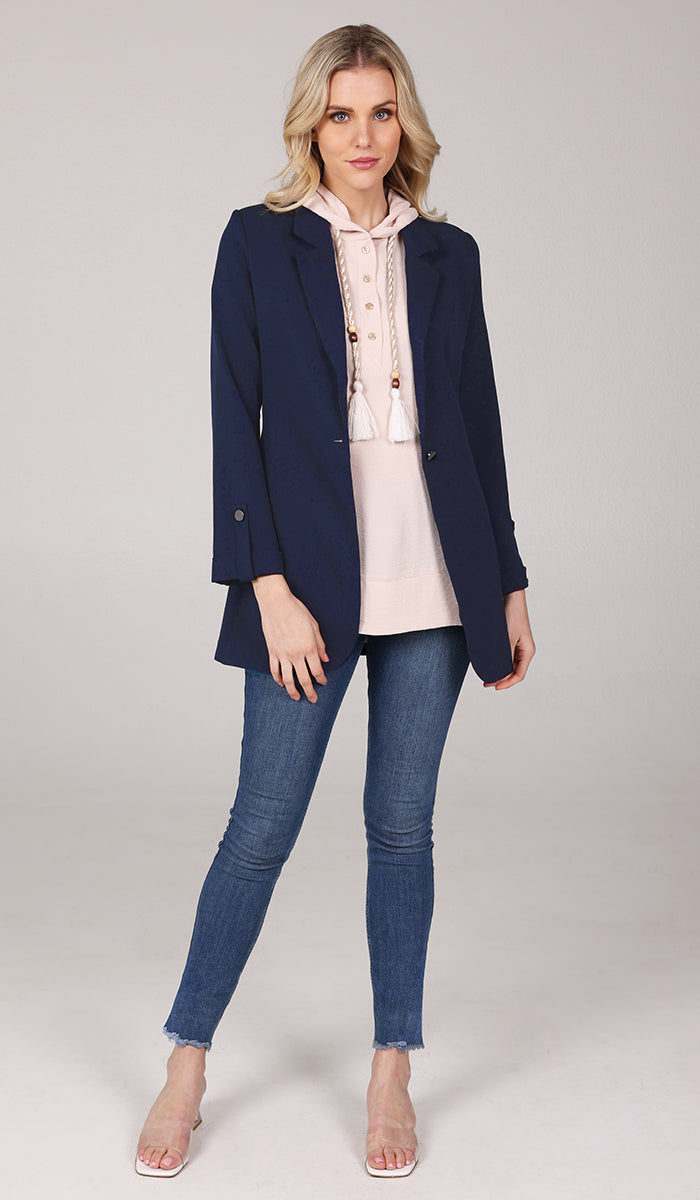 Front view of woman wearing a cream hoodie inside a navy blue blazer with blue jeans.