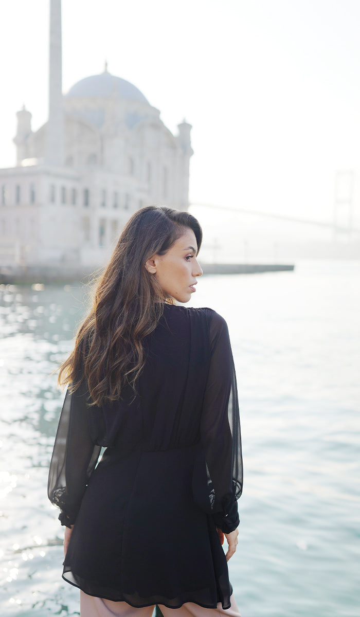 Back view of woman wearing Myra tunic in Black by the water. 