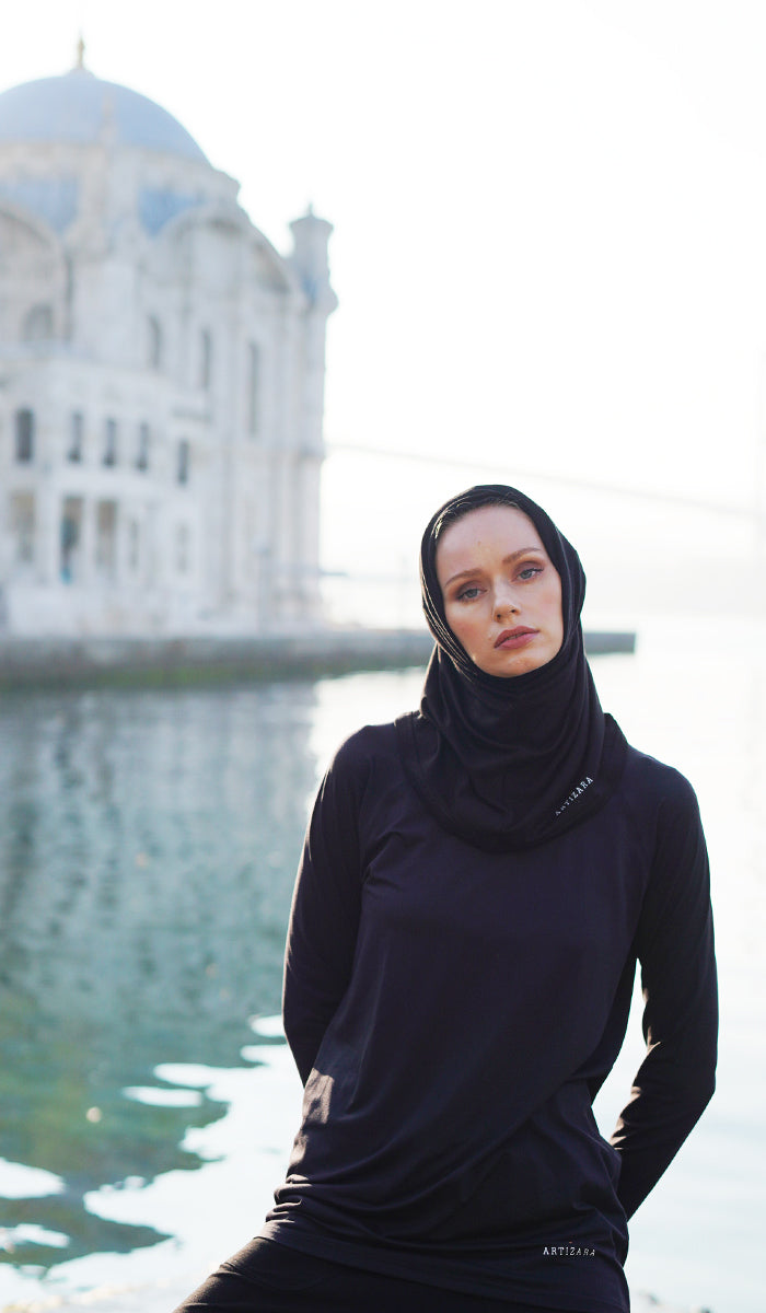 Woman by water wearing sports hijab in Black.