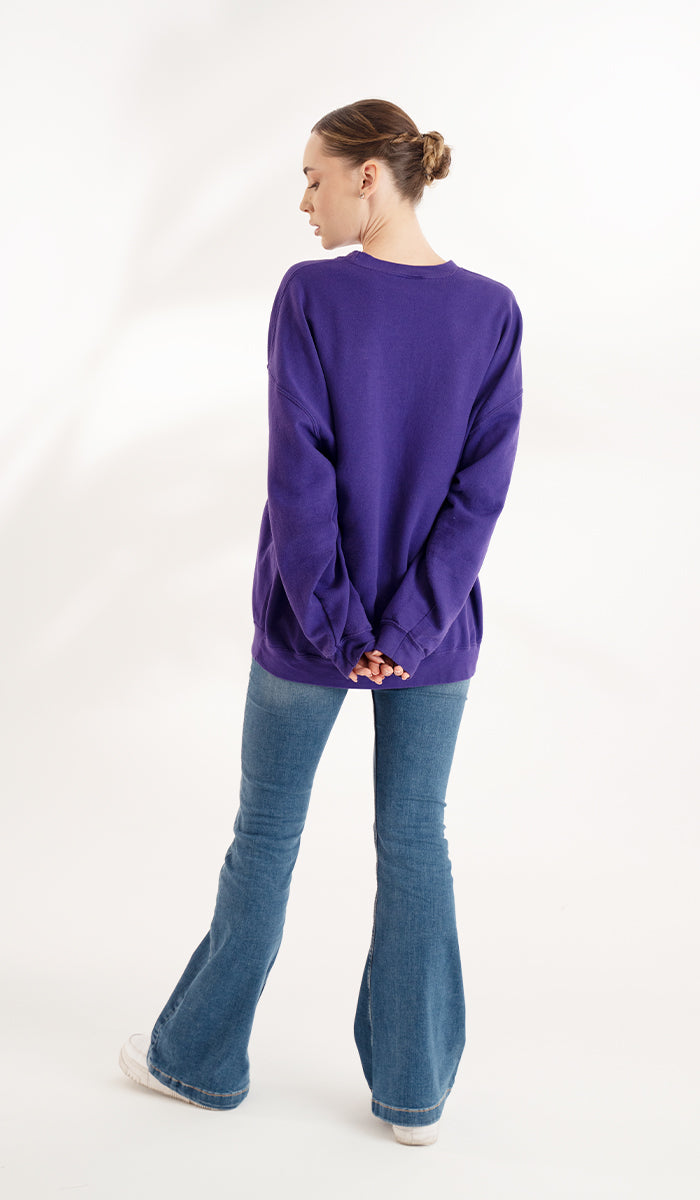 back view of a woman wearing a purple pullover sweater with jeans.