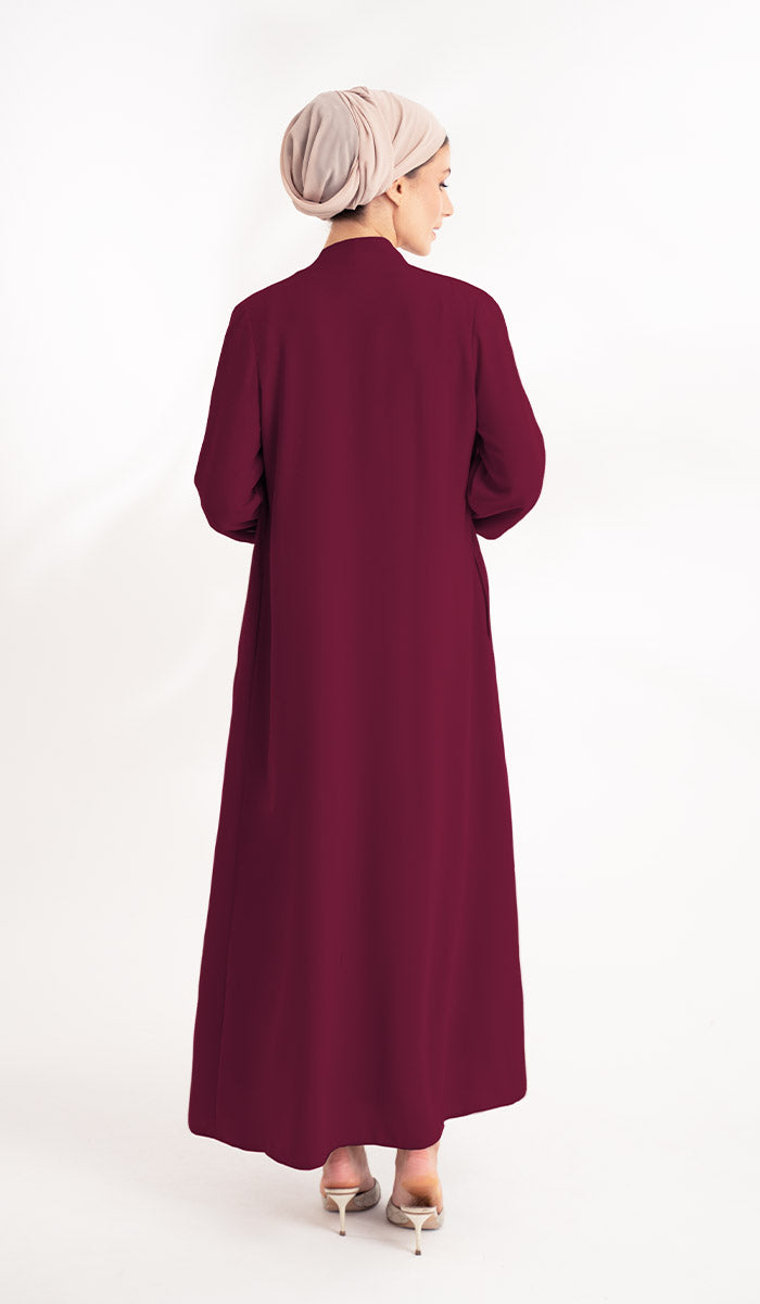 Back view of woman with beige turban wearing a long maroon duster jacket.