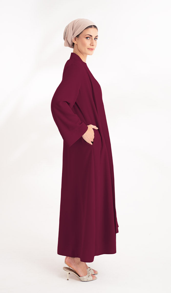 Woman with beige turban wearing a maroon duster jacket  with pockets..