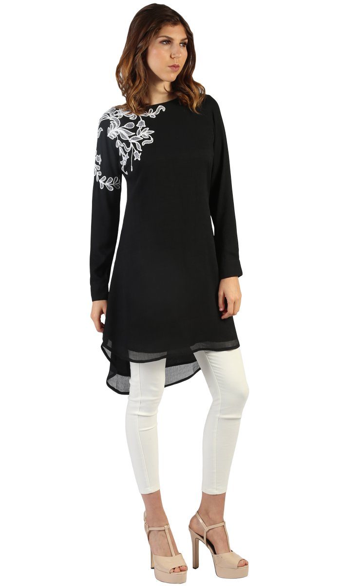 Woman at three-fourths angle wearing Selena tunic in Black with white pants and heels. 