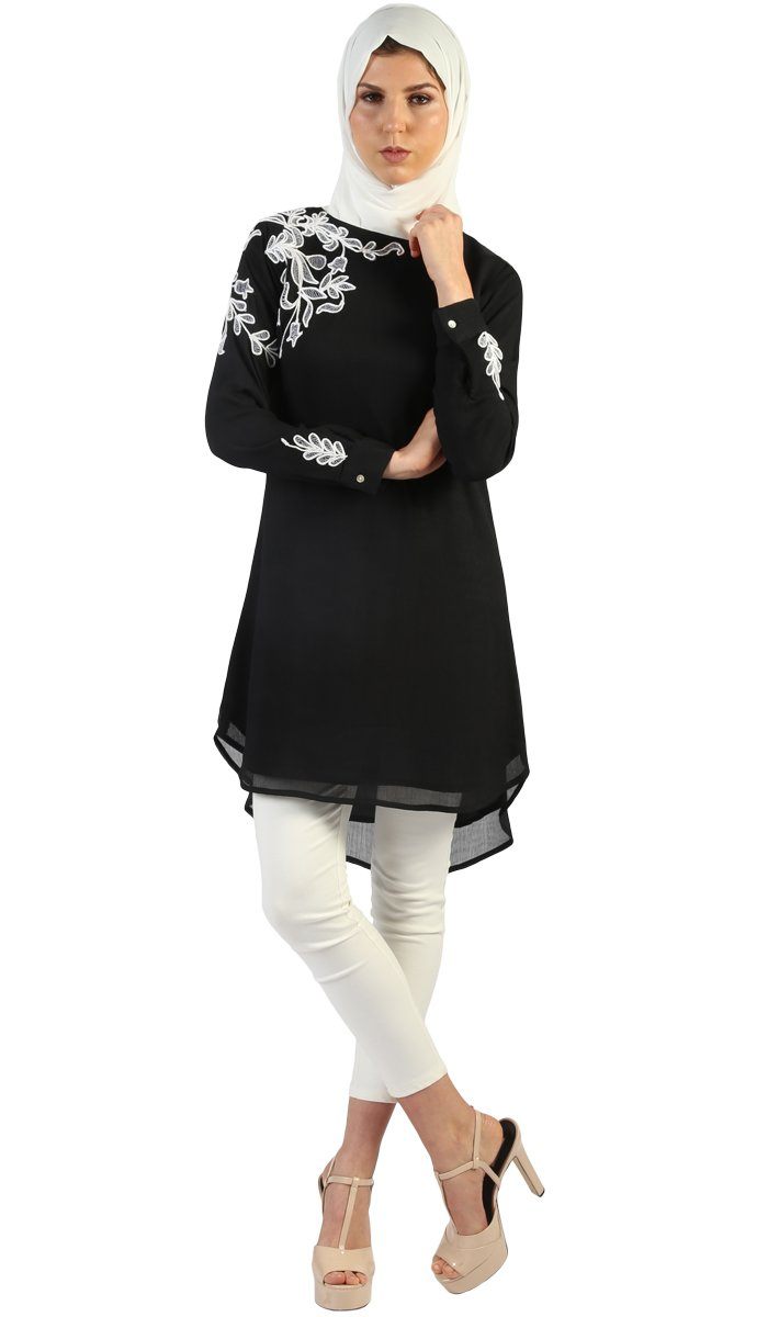 Woman with headscarf wearing Selena Embroidered Long Modest Tunic in Black with white pants and heels.