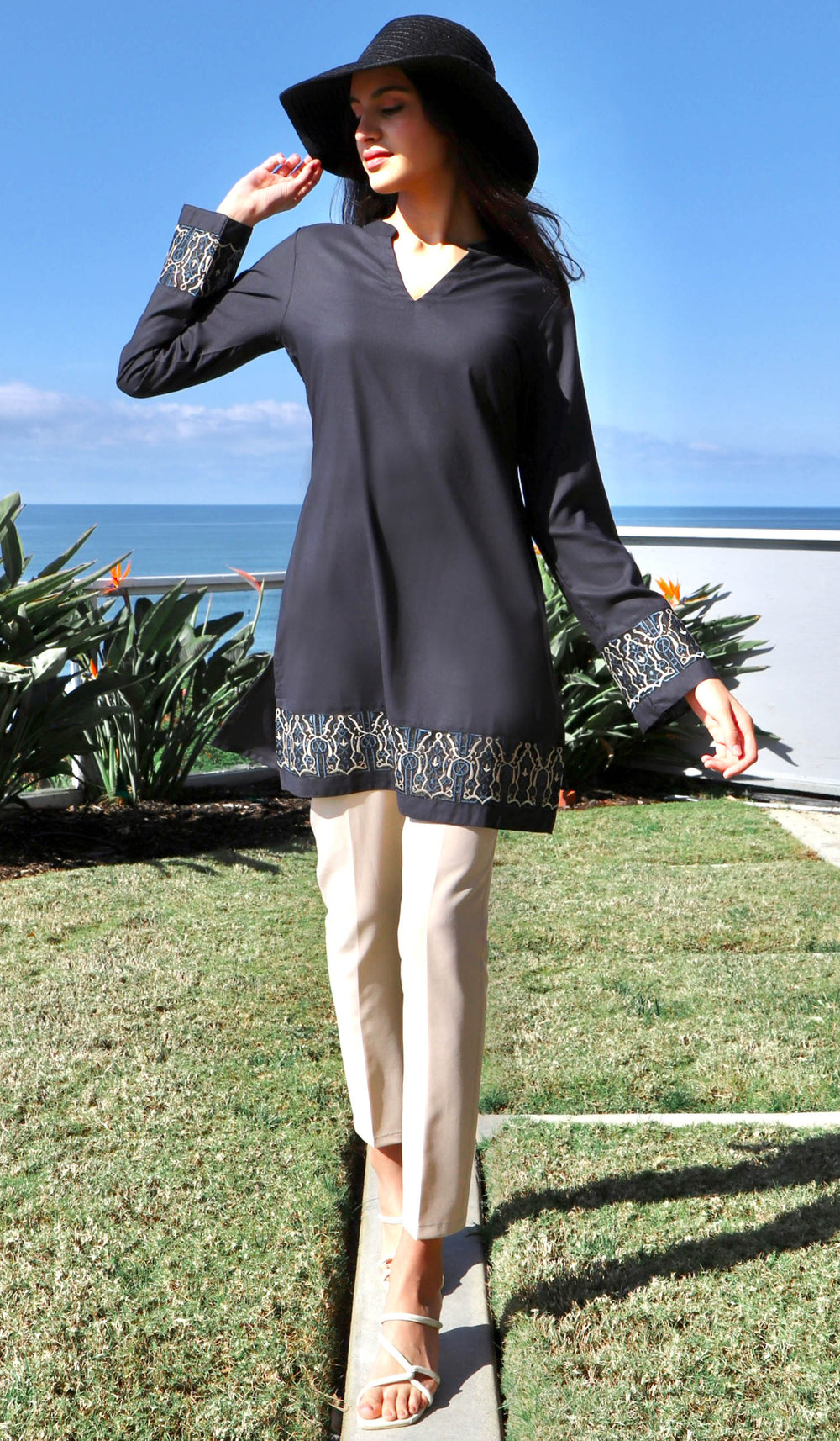 Woman outside wearing Selma tunic in Black with black hat, khaki pants and sandals. 