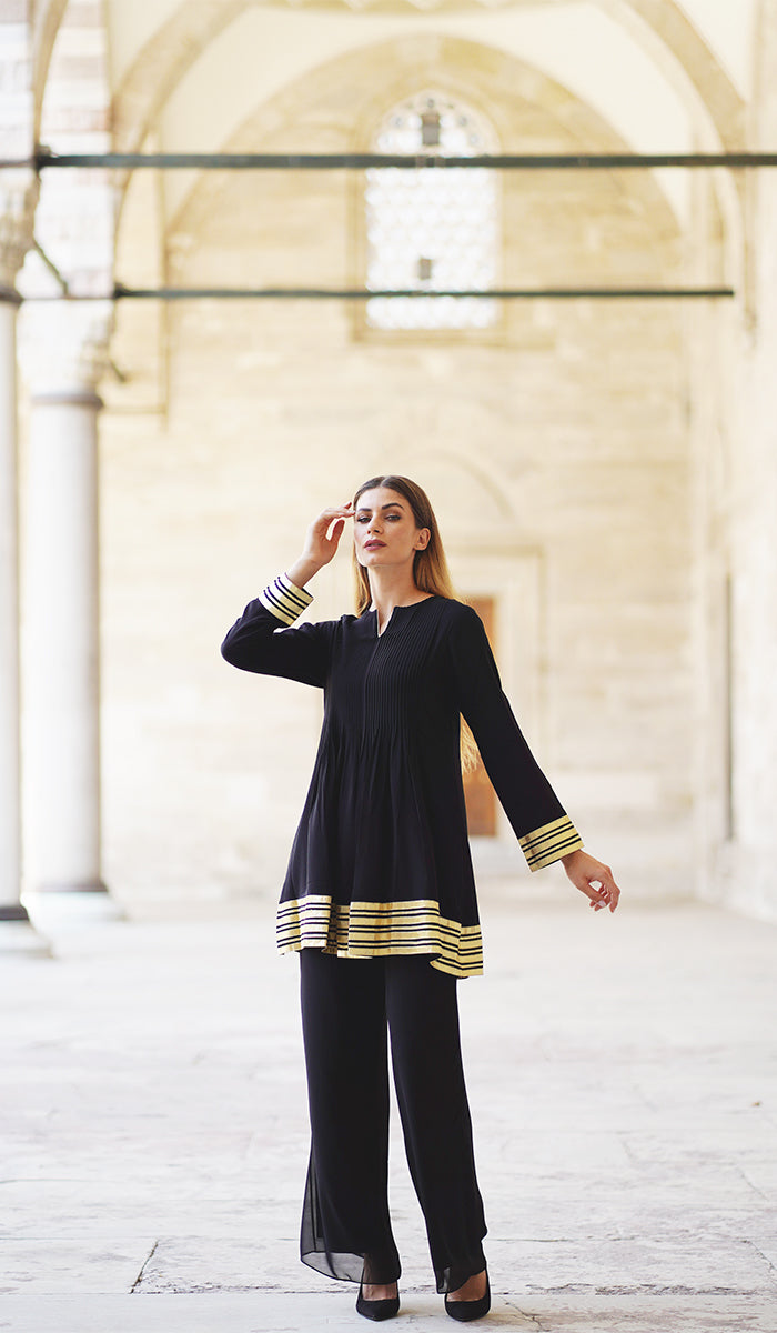 Woman in front of building wearing modest Sultana tunic in Black with black pants and heels. 