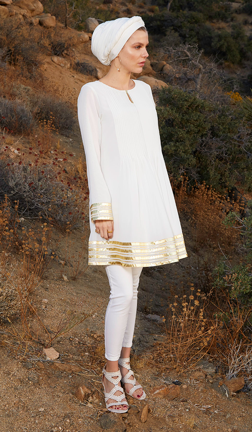 Side view of woman in hijab in the desert wearing Off White Sultana tunic with   white pants and heels. 